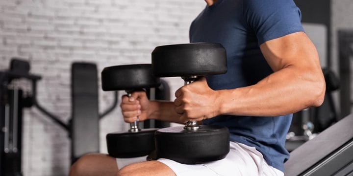 Holding two dumbbells while sitting on a bench, doing Hypertrophy program