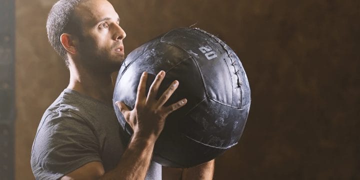 A buff male doing medicine ball exercises in the gym