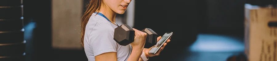 A teenager looking at her phone while lifting a dumbbell